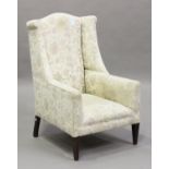 An Edwardian wing back armchair, the shaped back and arms upholstered in floral fabric, on square