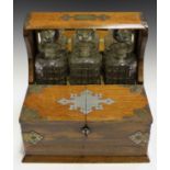 An Edwardian oak and brass mounted three-bottle tantalus, fitted with three glass decanters (