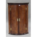 A George III oak hanging bowfront corner cabinet, crossbanded in mahogany and fitted with two doors,