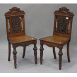 A pair of late Victorian oak hall chairs, the square panel backs carved with leaf scrolls, the solid