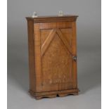 An Edwardian Arts and Crafts oak hanging wall cabinet, the bowed door with moulded panelling and