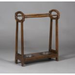 An early 20th century Arts and Crafts oak umbrella stand, the pierced ends united by turned supports