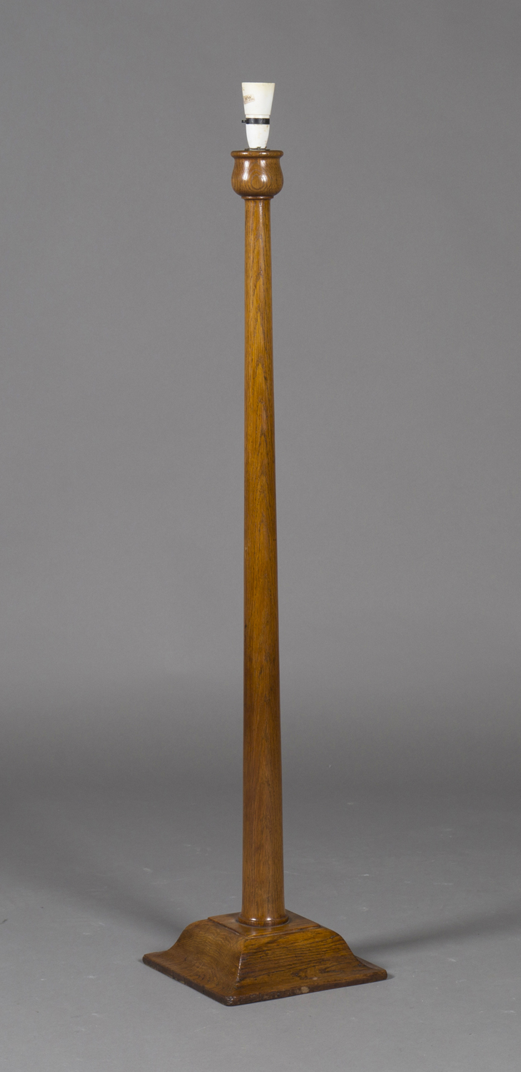 An early 20th century Arts and Crafts oak lamp standard, the tapering stem raised on a shaped square
