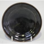 A Chinese dark brown/black glazed stoneware dish of shallow circular form, on an unglazed foot,