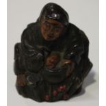 A Japanese lacquered horn netsuke, Meiji period, carved in the form of a seated figure holding a