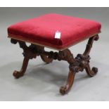 A Victorian mahogany 'X' framed stool, carved with foliate decoration, the seat overstuffed in red