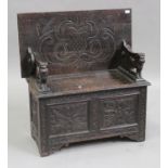 A Victorian oak monks bench with carved decoration, the lion mask armrests above a hinged seat and