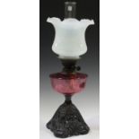 A late Victorian cast iron and cranberry glass table oil lamp with a vaseline glass shade with