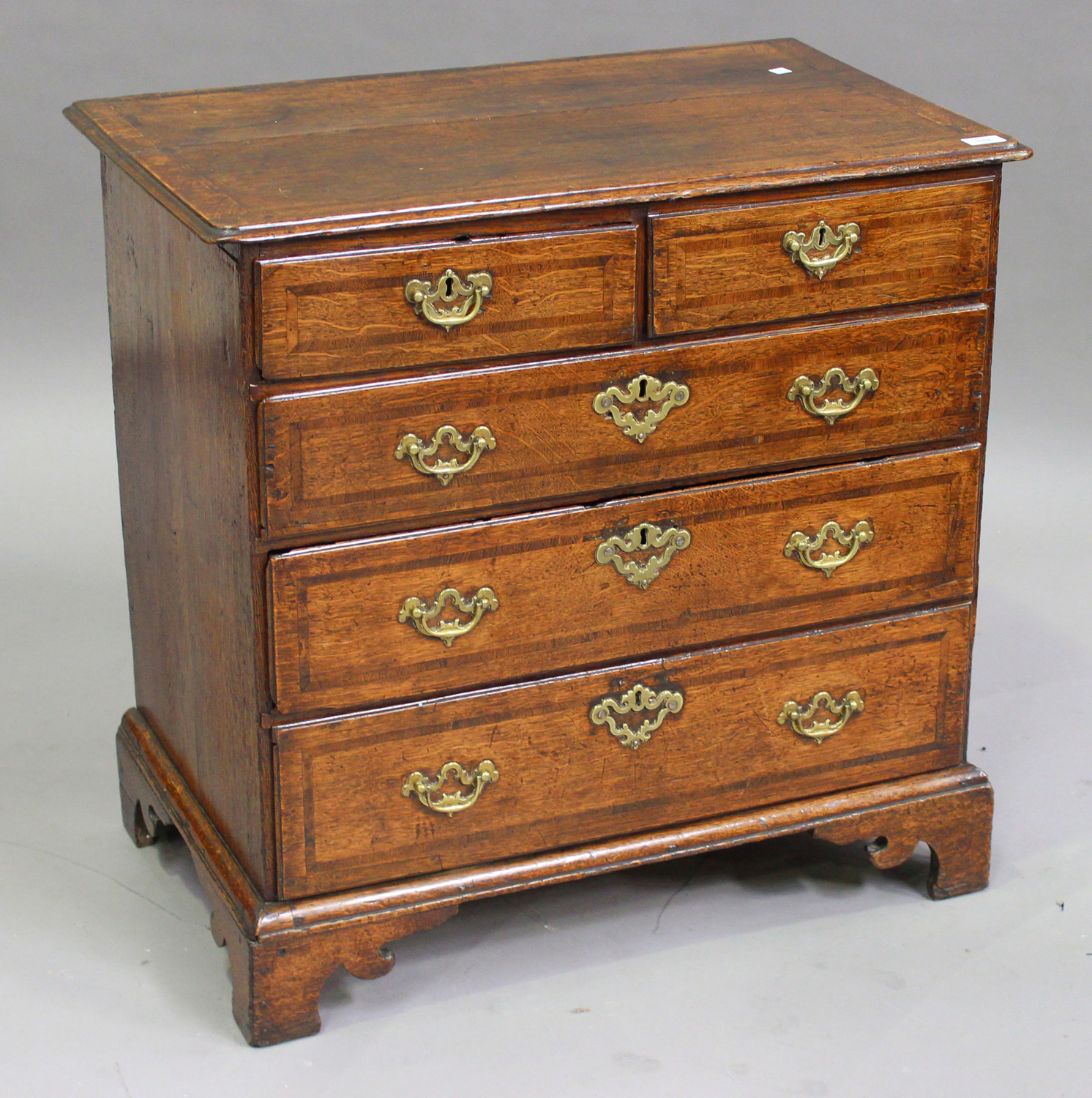 A small George II oak and mahogany crossbanded chest of two short and three long drawers, on