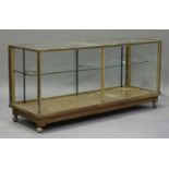 An Edwardian oak and brass mounted shop display counter, the glazed sliding doors enclosing glass
