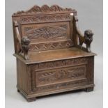 A Victorian carved oak box seat settle with lion mask armrests, the hinged seat above a panel front,