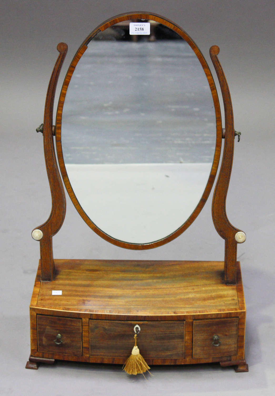 A George IV mahogany oval swing frame toilet mirror, the bowfront base fitted with three drawers, on