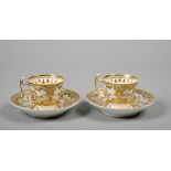 A pair of early 19c Spode embossed gilt and white cups and saucers, painted marks in red to base,