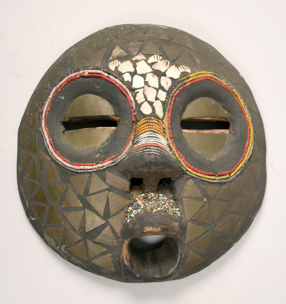 A 19c African coastal region carved wood mask, decorated with shells, 11.5in diam.