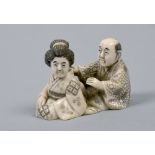 A Japanese carved ivory netsuke in the form of a lady and gentleman seated and observing, base