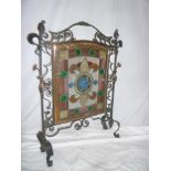 An unusual wrought iron and copper mounted fire screen with inset leaded glazed geometric panel