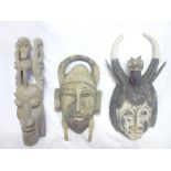 An African carved teak tribal mask with raised decoration and two other various carved tribal masks