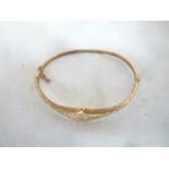 A 9ct gold oval bangle with engraved scroll decoration