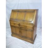 An Ercol medium elm bureau with two drawers in the frieze and cupboard enclosed by two panel doors