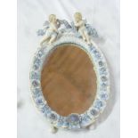 A Continental porcelain framed oval dressing mirror decorated in relief with flowers and cherubs,