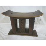 An old African Ashanti carved wood tribal stool with concave rectangular seat on carved supports