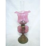 A Victorian brass oil lamp with cranberry tinted reservoir and cranberry tinted etched glass shade