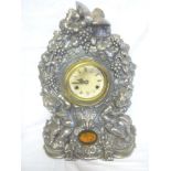 An unusual mantel clock with painted circular dial in white metal ornate arched case depicting