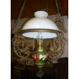An ornate brass and ceramic hanging oil lamp with floral decorated reservoir and opaque glass shade