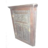 A 19th Century carved oak hanging corner cupboard with shelves enclosed by a decorated central door