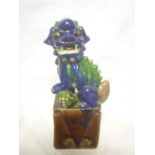 A Chinese temple dog figure with green and blue glazed decoration on brown rectangular stand.