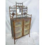 An old bamboo lacquered display cabinet with lined shelves enclosed by two glazed doors surmounted