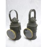 A pair of brass and painted metal railway hand lanterns with circular lenses and loop handles