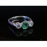 An 18ct white gold emerald and diamond ring the central emerald flanked by .20ct diamonds approx.