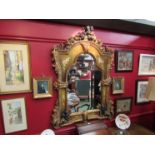 An ornate gilt framed mirror decorated with cherubs and floral oil panels,