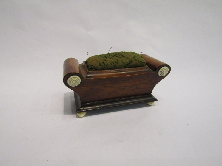 A 19th Century mahogany sarcophagus shape pin cushion with turned ivory feet and roundel decoration,