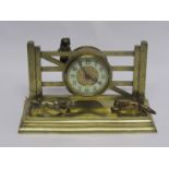 An early 20th Century brass novelty timepiece in the form of two dogs chasing a fox near a gate,