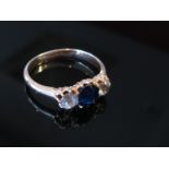 A gold ring with central blue sapphire flanked by white sapphires, unmarked, size M/N, 3.