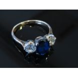 A gold and platinum set sapphire and diamond ring the central blue oval sapphire flanked by .