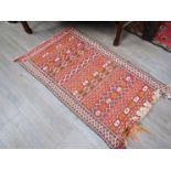 A small loom-woven rug worked in ochre, red, cream and brown with stripes.