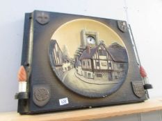 A ceramic wall plaque on a back board with inset clock.