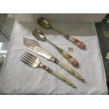 A pair of fish servers with carved horn handles and a pair of salad servers with ceramic handles.