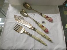 A pair of fish servers with carved horn handles and a pair of salad servers with ceramic handles.