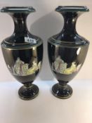 A pair of black glazed vases depicting classical scenes.