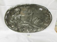 An oval white metal plaque depicting harpist with swan.