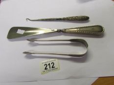 A silver handled button hook, a silver handled shoe horn and silver sugar tongs.