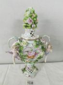 A 19th century porcelain lidded urn encrusted with flowers and surmounted 2 cherubs, 31 cm tall.