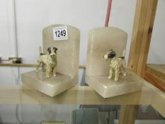 A pair of alabaster bookends surmount cold painted terrier dogs (one dog need re-fixing).