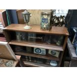 A bookcase full of an interesting collection of items including brassware, tins, bell, silverplate,