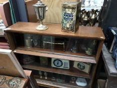 A bookcase full of an interesting collection of items including brassware, tins, bell, silverplate,