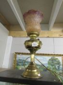 A brass electric table lamp in the form of an oil lamp with shade and chimney.